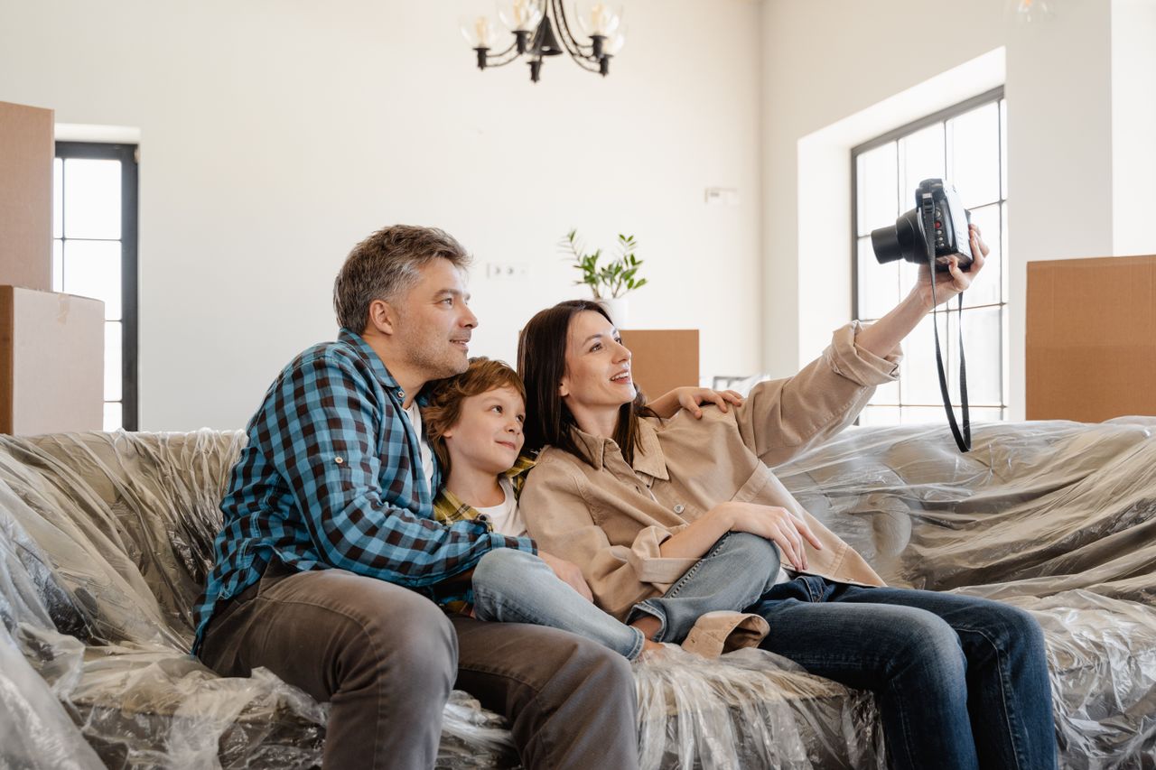 About Family taking a selfie on moving day, sitting on a couch amidst packed boxes.