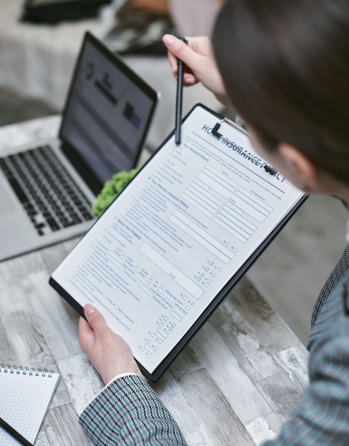 An adult reviews a home insurance policy document at a desk with a pen and laptop.