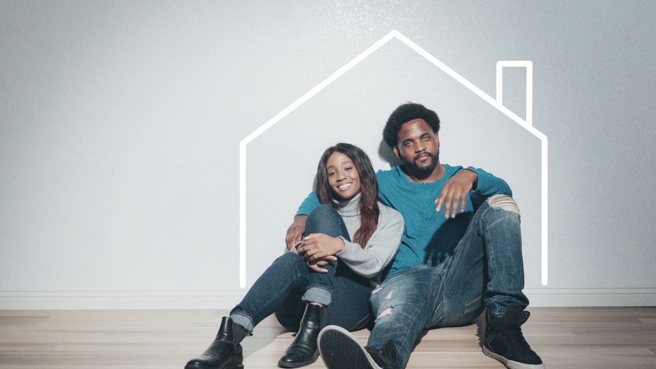 Services A joyful couple sitting indoors with a house outline, symbolizing their new home.